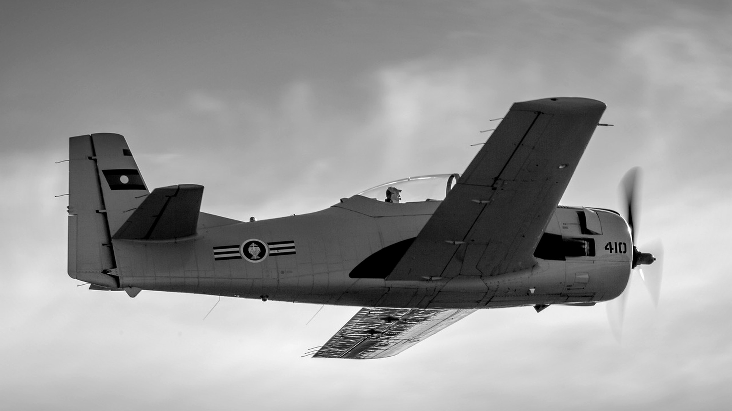 A Trojan aircraft banking in flight, tail number 410, shot in black and white